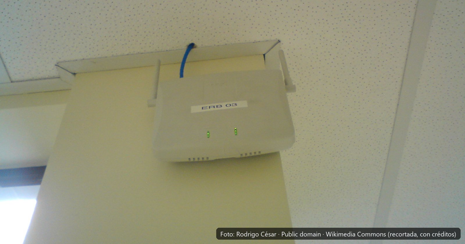 Punto de acceso inalámbrico instalado en la parte alta de una pared, junto al techo de una oficina